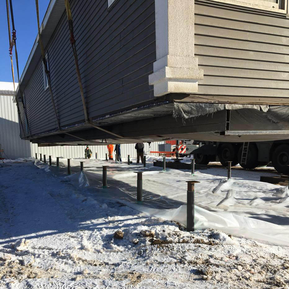 A manufactured home being lowered onto screw piles with a crane
